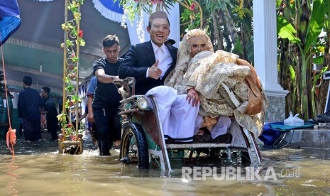 Pengantin naik becak usai resepsi pernikahan di tengah genangan air banjir di Desa Jatigedong, Kecamatan Ploso, Kabupaten Jombang, Jawa Timur, Rabu (1/5/2019).