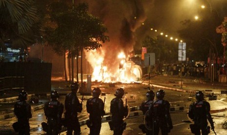 Riot police stand guard as a vehicle goes up in flames after a riot broke out in Singapore's Little India, Sunday (8/12).