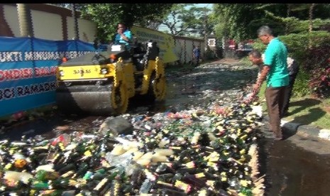 Sebuah alat berat, sedang memusnahkan ribuan botol miras hasil razia 