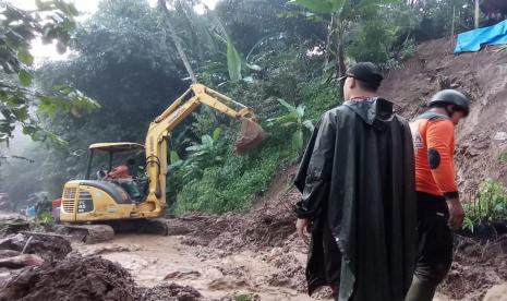 Sebuah alat pengeruk tanah milik BPBD membersihkan material longsor yang menutup akses jalan penghubung. 