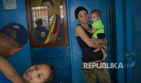 Sebuah keluarga bermain di ruang tamu rumah mereka, dihiasi dengan potret mendiang Presiden Venezuela Hugo Chavez, di Caracas, Venezuela, Kamis (7/2/2019).