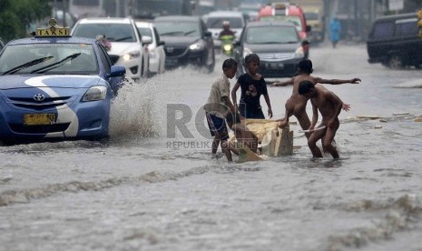   Sejumlah anak bermain air saat banjir di Jalan Gunung Sahari, Jakarta, Ahad (12/1). (Republika/Agung Supriyanto)