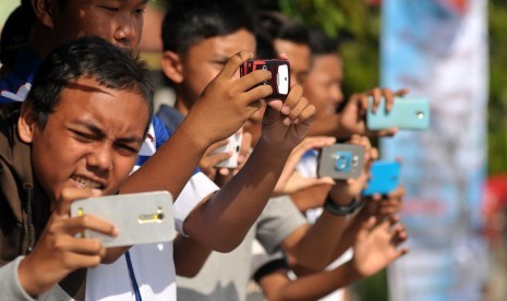  Sejumlah anak mengoperasikan telepon genggam saat menunggu bus yang membunyikan klakson telolet melintas di jalur Pantura, Brebes, Jawa Tengah, Rabu (21/12).