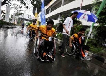 Sejumlah atlet disabilitas Malaysia berjalan menembus hujan yang mengguyur kawasan arena Atletik ASEAN Para Games (APG) VI saat tiba di Stadion Manahan, Solo, Jawa Tengah, Selasa (13/12). 