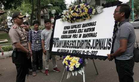 Sejumlah jurnalis menyerahkan karangan bunga duka cita kepada Kapolres Banyumas AKBP Bambang Yudhantara Salamun (kiri) saat melakukan aksi unjuk rasa, di Pendopo Bupati Banyumas, Jawa Tengah, Selasa (10/10). Elemen jurnalis di Kabupaten Banyumas mengutuk tindak kekerasan oleh polisi dan Satpol PP terhadap sejumlah wartawan saat meliput pembubaran unjuk rasa penolakan pembangunan PLTPB Baturraden pada Senin (9/10) malam.