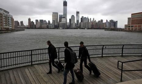  Sejumlah orang berjalan membawa tas mereka dengan latar belakang gedung pencakar langit di Waterfront,New Jersey, Ahad (28/10) waktu setempat.    (Eduardo Munoz/Reuters)