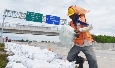 Sejumlah pekerja membuat tanggul dengan karung berisi pasir di tepi jalan tol Trans Jawa ruas Ngawi-Kertosono pada kilometer 603-604 yang sebelumnya terendam banjir di Desa Glonggong, Balerejo, Kabupaten Madiun, Jawa Timur, Sabtu (16/3/2019). 