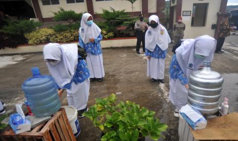 Sejumlah pelajar mencuci tangannya sebelum masuk ke sekolah dengan pengawasan dari petugas kepolisian dan Satpol-PP di SMPN 1 Kota Padangpanjang, Sumatera Barat, Kamis (13/8/2020). Pemkot Padangpanjang yang daerahnya termasuk zona kuning membuka sekolah tatap muka pertama untuk jenjang SMP dengan tetap mematuhi protokol kesehatan COVID-19 dan pelaksanaan secara bergantian yaitu sehari di sekolah dan sehari belajar di rumah.