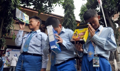 Sejumlah pelajar mengamati pergerakan sinar matahari menggunakan teropong kardus bekas saat dilakukan percobaan pembuatan teropong gerhana matahari di SD Muhammadiyah I Magelang, Temanggung, Jawa Tengah, Senin (7/3). 