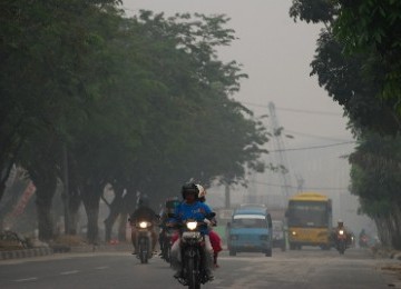 Sejumlah pengendara menyalakan lampu ketika melintas di tengah kabut asap di Pekanbaru, Riau, Ahad (10/7). 