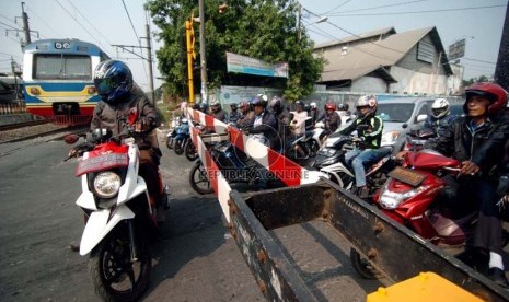 Sejumlah pengendara sepeda motor menunggu di depan pintu perlintasan kereta api kawasan Kalibata, Jakarta Selatan.( Republika/Raisan Al Farisi)