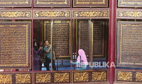 Sejumlah pengunjung berfoto di Alquran raksasa di Gandus, Palembang, Sumatera Selatan, Sabtu (3/6). Keberadaan Alquran raksasa (Alquran AL-Akbar) yang diukir di atas kayu trembesi itu menjadi destinasi wisata religi di Palembang. 