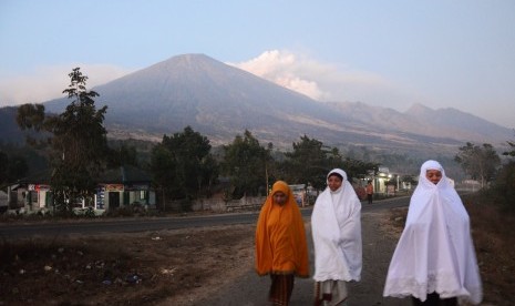 Sejumlah perempuan berjalan dengan latar belakang debu vulkanik Gunung Barujari yang menyembur dibalik puncak Gunung Rinjani di Desa Sembalun Lawang, Kecamatan Sembalun, Selong, Lombok Timur, NTB, Selasa (10/11).