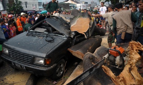 Sejumlah petugas berusaha memotong batang pohon yang tumbang menimpa kendaraan setelah hujan deras dan angin kencang di kawasan Pasir Koja, Bandung, Jawa Barat, Rabu (9/12).