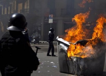 Sejumlah polisi Spanyol berdiri dekat tong sampah terbakar. Terjadi bentrok antar massa protes dengan aparat dan aksi kekerasan dalam demonstrasi yang berujung rusuh di Barcelona