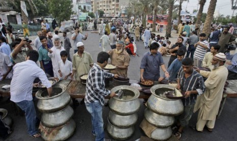  Sejumlah pria Pakistan membagikan piring makanan kepada jamaah yang hendak berbuka puasa di Karachi, Pakistan, Sabtu (21/7).  (Shakil Adil/AP)