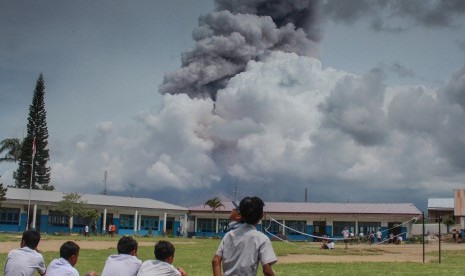 Sejumlah siswa bermain di halaman sekolah dengan latar belakang Gunung Sinabung yang mengeluarkan material vulkanik, di desa Ndokum Siroga, Karo, Sumatera Utara, Selasa (11/4).