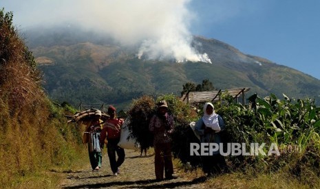 Sejumlah warga berjalan di areal perladangan berlatar belakang kebakaran hutan gunung Sumbing di Desa Adipura, Kaliangkrik, Magelang, Jawa Tengah, Rabu (14/8/2019). 