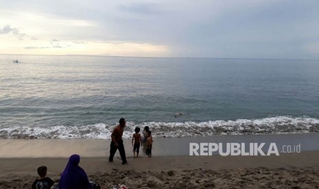 Sejumlah warga bermain air di Pantai Duduk, Kecamatan Batulayar, Kabupaten Lombok Barat, NTB pada Ahad (26/11) sore. Tampak dari kejauhan terlihat pemandangan Gunung Agung di Bali yang terlihat gelap.