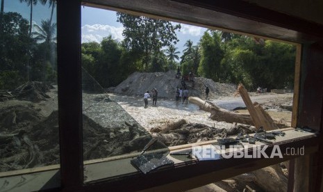 Sejumlah warga melintas di depan rumah yang tertimbun lumpur akibat banjir bandang di Desa Bangga, Sigi, Sulawesi Tengah. (Dok)