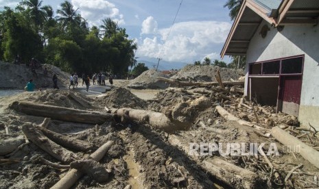 Sejumlah warga melintas di depan rumah yang tertimbun lumpur akibat banjir bandang di Desa Bangga, Sigi, Sulawesi Tengah, Jumat (23/11/2018).