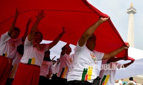 Sejumlah warga membentangkan bendera Merah-Putih dalam Festival Damai dan Millennial Safety Road di Monas, Jakarta Pusat, Ahad (23/6/2019). 