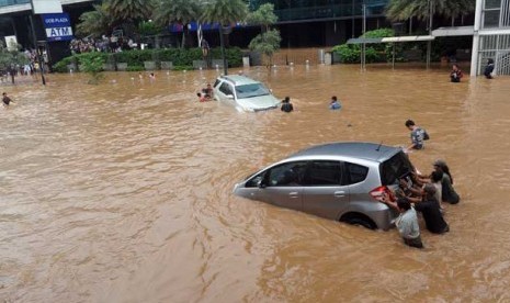 Sejumlah warga mendorong mobil yang terjebak banjir di kawasan Jl. Sudirman, Jakarta, Kamis (17/1).