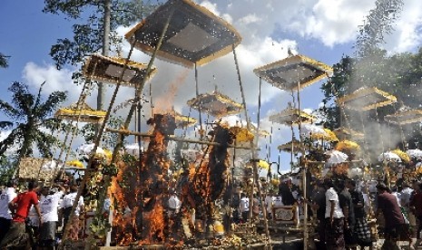 Sejumlah warga menyaksikan pembakaran peti mati berbentuk singa dan sapi yang berisi jenazah anggota keluarganya dalam Ngaben massal di Desa Kedewatan, Ubud, Bali, Minggu (18/8). 