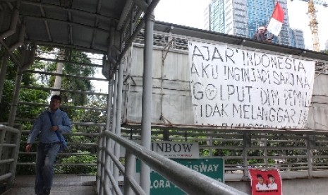 Seorang aktivis mengibarkan bendera merah putih dan membentangkan sepanduk ajakan Golput di atas Jembatan Penyebrangan Orang (JPO) di Jalan Jendral Sudirman, Jakarta Pusat, Jumat (4/7).