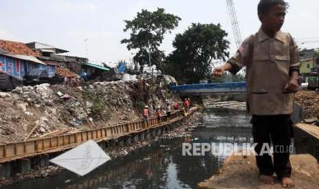 Seorang anak bermain layang-layang saat pekerja menyelesaikan pembangunan turap di sepanjang Kali Grogol, Palmerah Barat, Jakarta, Rabu (5/9). 