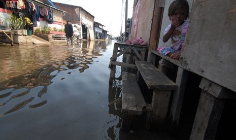 Seorang anak duduk di depan rumahnya yang terkena banjir rob (air laut pasang), di Dadap, Kabupaten Tangerang, Banten, Senin (23/11).