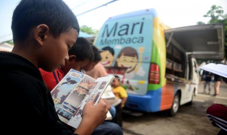 Seorang anak embaca buku di perpustakaan keliling.