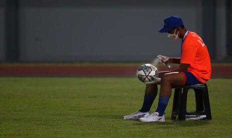 Seorang anak gawang menyemprotkan cairan disinfektan ke bola yang digunakan dalam pertandingan BRI Liga 1. Laga Liga 1 antara Persib vs Barito Putera.