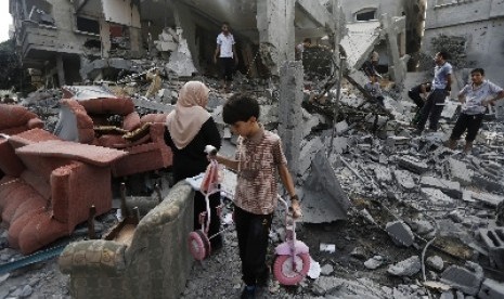 Seorang anak kecil berjalan di antara reruntuhan bangunan di Jalur Gaza yang dihantam roket militer Israel.