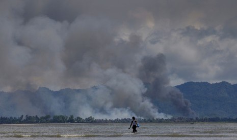 Seorang anak laki-laki Bangladesh berjalan menuju kapal saat asap terlihat dari seberang perbatasan di Myanmar, di Shah Porir Dwip, Bangladesh. Menggambarkan kekerasan sedang berlangsung di Myanmar dan menunjukkan banyak rumah Rohingya yang dibakar, Kamis (14/9).