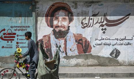 Seorang anak laki-laki menjajakan melewati lukisan dinding dengan potret tokoh Mujahidan dari Lembah Pansjshir, mendiang komandan Afghanistan Ahmad Shah Massoud di Kabul pada 8 September 2021. 