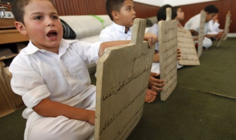 Seorang anak membaca sebuah papan tulis kayu sambil menghafal Alquran di Tripoli, Libya, Senin (23/7).   (Ismail Zitouny/Reuters)