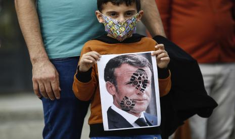 Sentimen Anti-Prancis Menguat di Sejumlah Negara Muslim. Seorang anak memegang foto Presiden Prancis Emmanuel Macron, dicap dengan tanda sepatu, selama protes terhadap Prancis di Istanbul, Minggu, 25 Oktober 2020. Presiden Turki Recep Tayyip Erdogan pada hari Minggu menantang Amerika Serikat untuk menjatuhkan sanksi terhadap negaranya sekaligus meluncurkan serangan kedua terhadap Presiden Prancis Emmanuel Macron. Berbicara sehari setelah dia menyarankan Macron membutuhkan perawatan kesehatan mental karena sikapnya terhadap Islam dan Muslim, yang mendorong Prancis menarik duta besarnya untuk Ankara, Erdogan membidik kritik asing