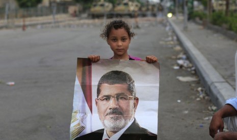   Seorang anak memegang poster Presiden Muhammad Mursi tidak jauh dari gedung Pengawal Republik di Nasr City, Kairo, Rabu (10/7).   (AP/Hassan Ammar