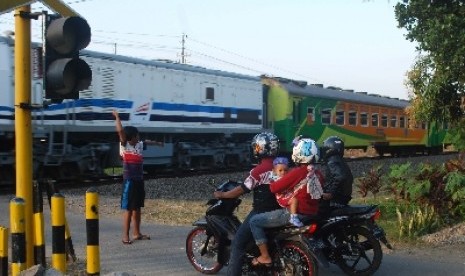 Seorang anak mengatur lalu lintas ketika ada kereta yang melintas di sebuah perlintasan kereta api. 