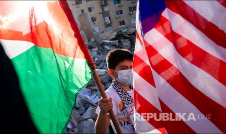 Seorang anak mengibarkan bendera Palestina disamping reruntuhan gedung Al Jalaa yang hancur oleh serangan udara Israel, Gaza, Jumat (21/5) waktu setempat.  Sejumlah media internasional menempati gedung Al-Jalaa termasuk kantor berita Associated Press yang telah berkantor disana selama 15 tahun.