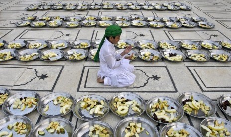   Seorang anak Pakistan berdoa diantara deretan piring berisi buah yang disumbangkan untuk jamaah yang hendak berbuka puasa di sebuah masjid di Karachi, Pakistan, Sabtu (21/7).  (Shakil Adil/AP)