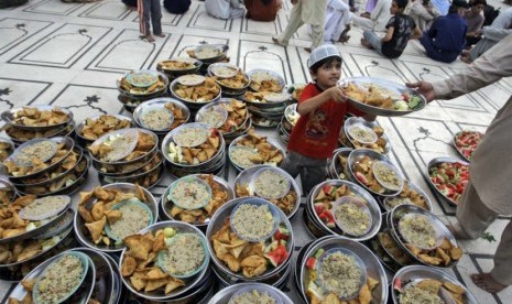  Seorang anak Pakistan membagikan piring makanan kepada jamaah yang hendak berbuka puasa di sebuah masjid di Karachi, Pakistan, Sabtu (21/7).  (Shakil Adil/AP)