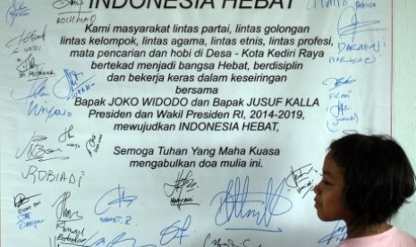 Seorang anak perempuan melihat spanduk yang berisi dukungan elemen masyarakat dan tanda tangan dukungan pasangan capres Jokowi-JK di Kediri, Jawa Timur, Ahad (15/6). 