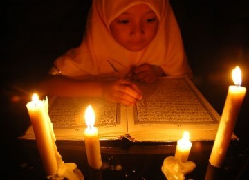 Seorang anak sedang membaca ayat suci Alquran mengunakan lilin/ilustrasi 