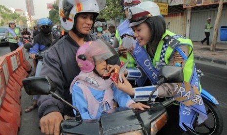 Seorang anggota kepolisian memasangkan pengikat helm pengendara motor yang tidak terpasang di Surabaya, Jawa Timur, Selasa (27/10). 