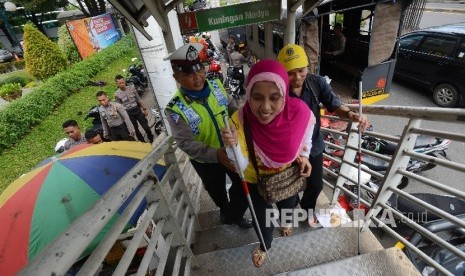  Seorang anggota kepolisian menuntun pasangan suami istri penyandang disabilitas untuk menyeberangi Jembatan Penyeberangan Orang (JPO) di Jalan Rasuna Said, Jakarta Selatan, Rabu (13/4).   (Republika/Raisan Al Farisi)