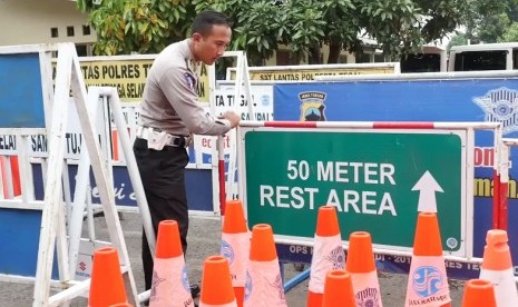 Seorang anggota polisi sedang merapihkan marka jalan dan rambu lalu lintas.