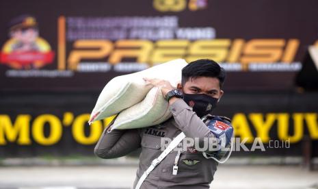 Seorang anggota Polri mengangkat beras bantuan sosial kepada masyarakat yang membutuhkan (ilustrasi).