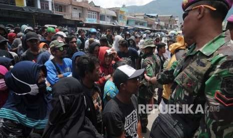 Seorang anggota TNI menertibkan antrean korban gempa dan tsunami untuk mendapatkan bantuan di salah satu Posko di Palu, Sulawesi Tengah, Ahad (7/10).